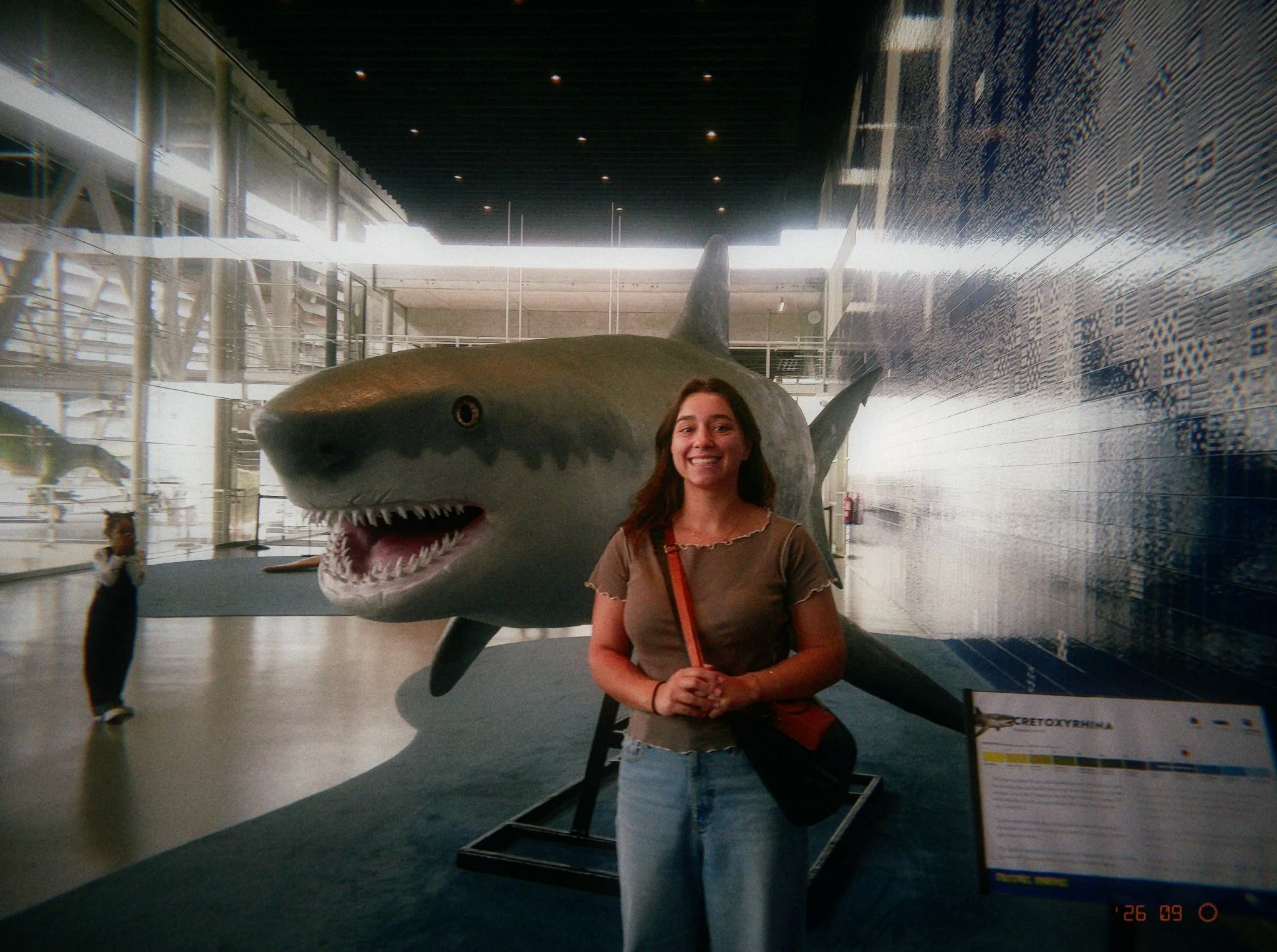 Júlia smiling beside a large shark exhibit